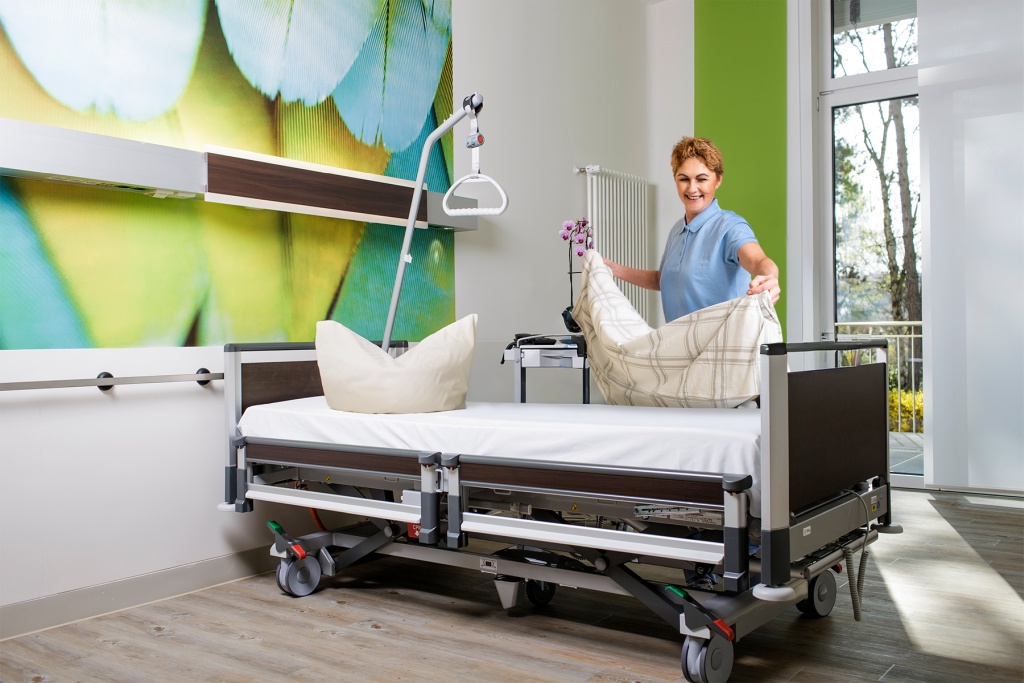 Eine Mitarbeiterin von RWS Gebäudeservice richtet ein Patientenbett in einem hellen Krankenzimmer her.