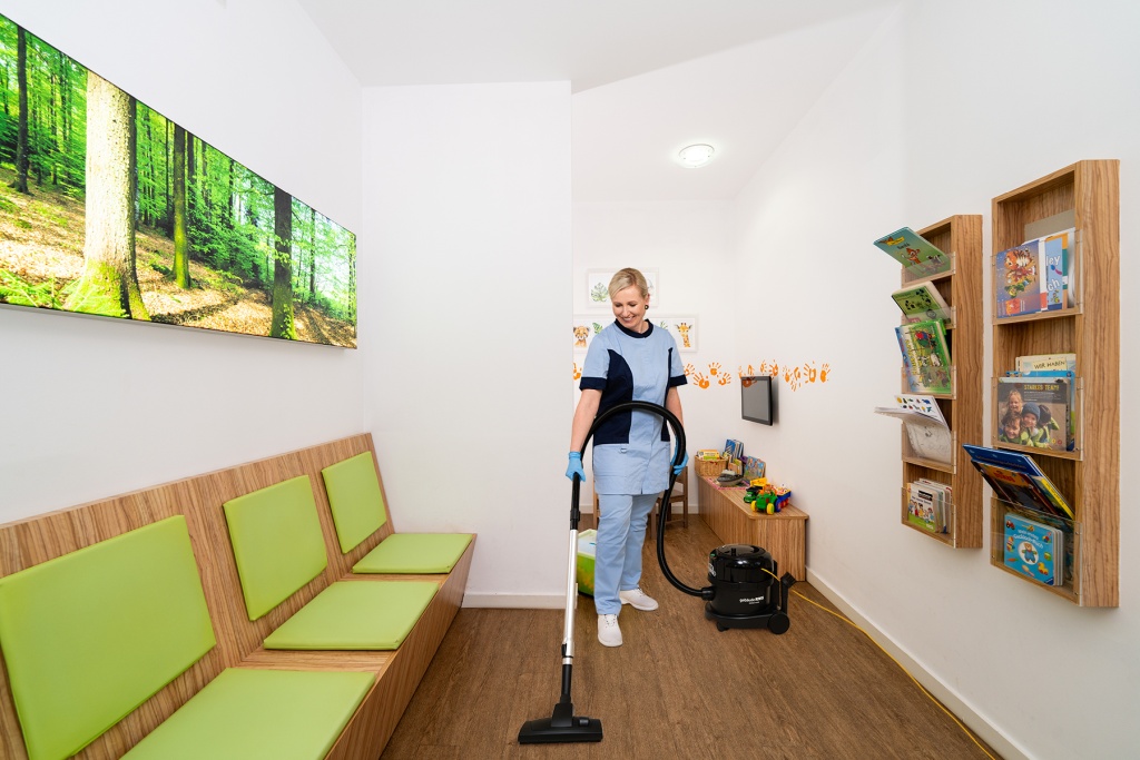 RWS Gebäudeservice Mitarbeiterin saugt Wartezimmer in medizinischem Versorgungszentrum für hygienische Sauberkeit.