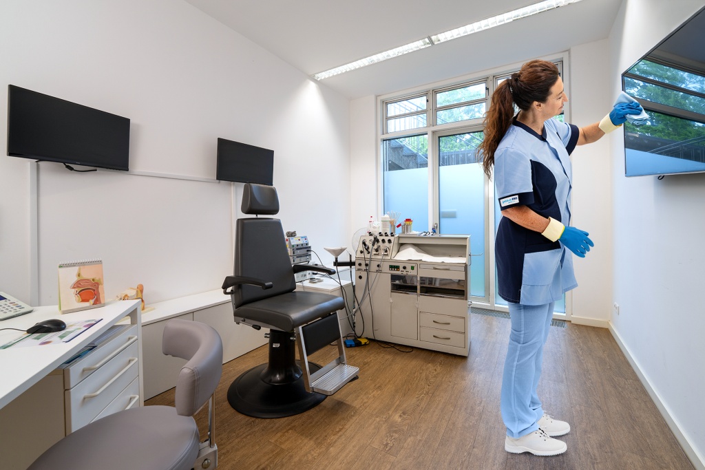 RWS Gebäudeservice Mitarbeiterin reinigt Oberflächen in Behandlungsraum einer Arztpraxis für maximale Hygiene.