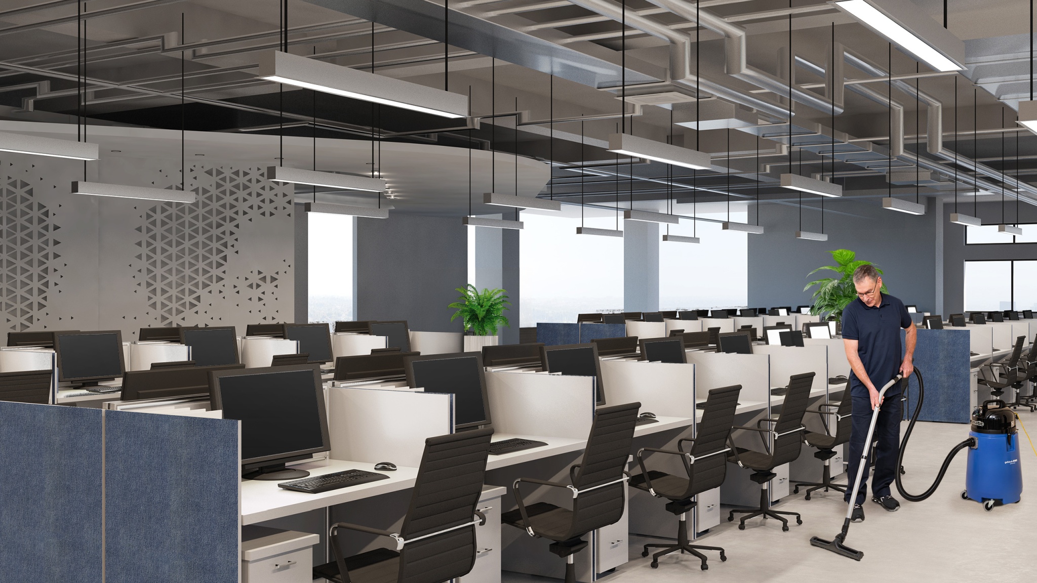 Mitarbeiter reinigt mit einem Staubsauger den Boden in einem modernen Großraumbüro mit vielen Arbeitsplätzen und Monitoren.
