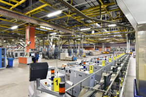 Große Produktionshalle mit Maschinen, Förderanlagen und nummerierten Arbeitsstationen.
