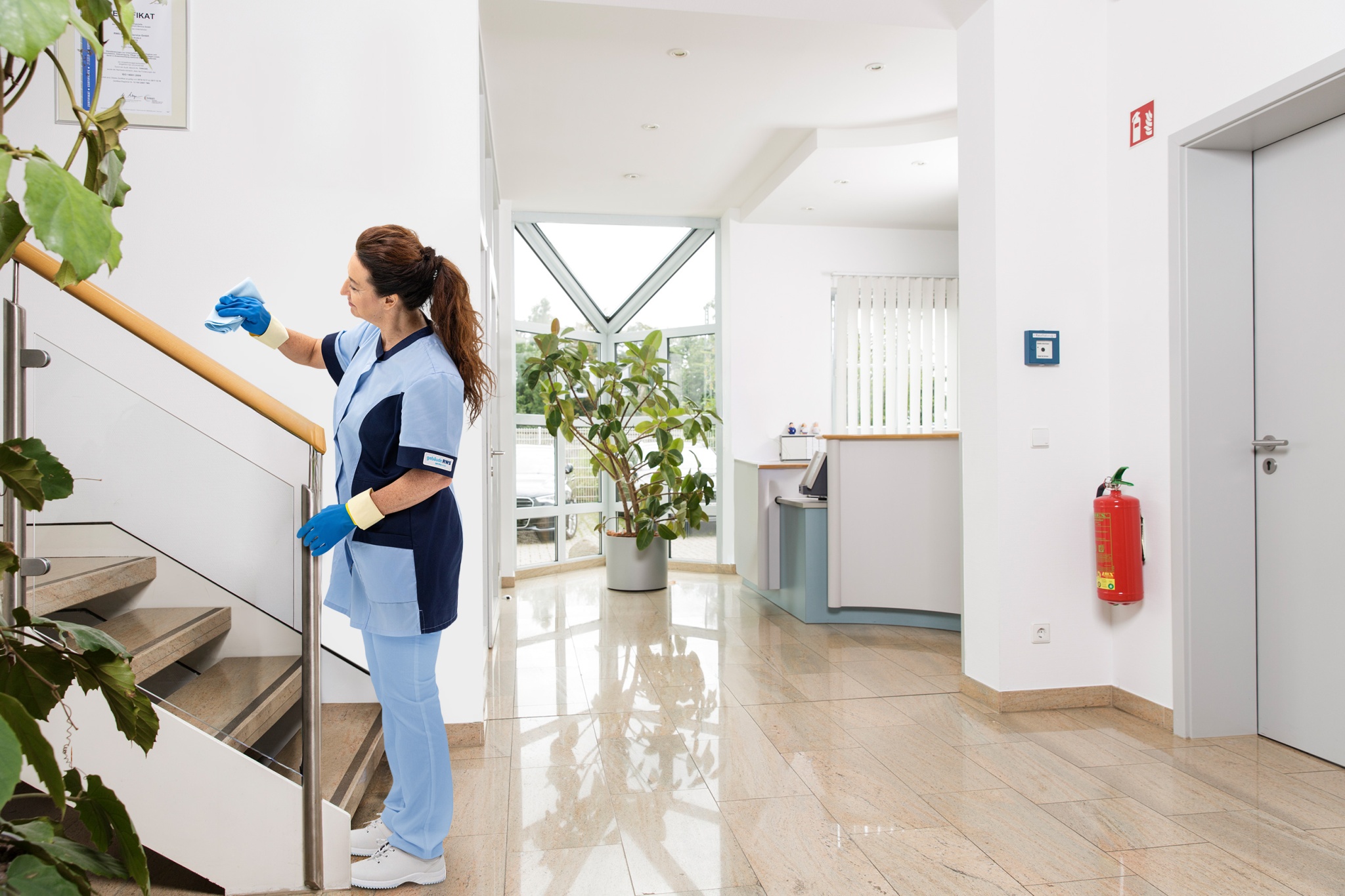 Mitarbeiterin von RWS Gebäudeservice reinigt das Treppengeländer im Eingangsbereich eines Bürogebäudes.