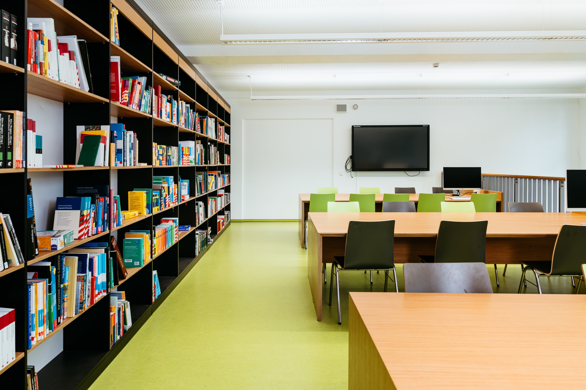 Moderne Schulbibliothek mit Bücherregalen, Tischen und digitalen Arbeitsplätzen