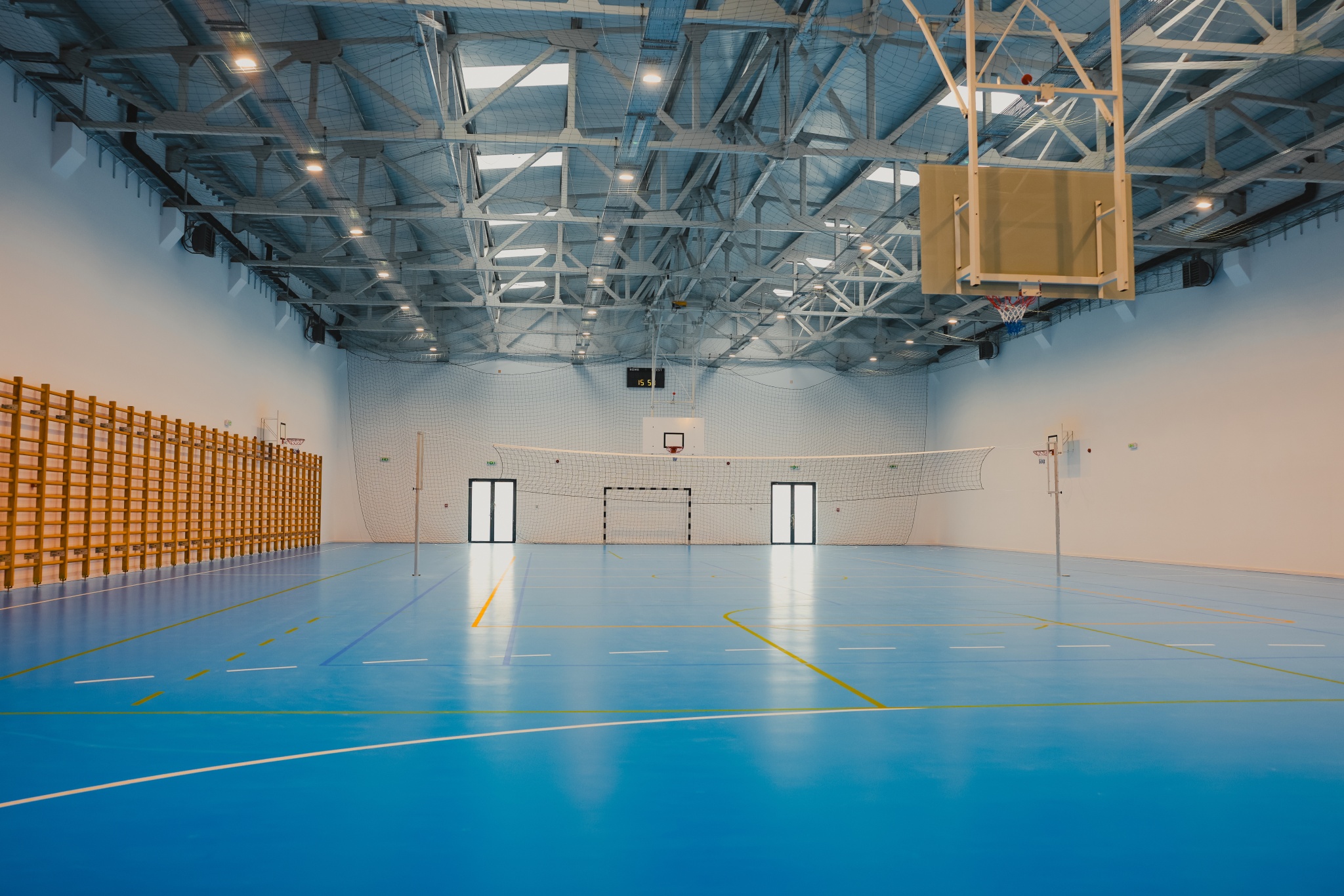 Moderne Sporthalle mit blauen Spielfeldern, Basketballkörben und Volleyballnetz