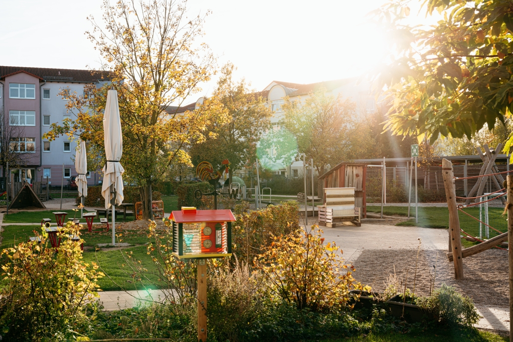 Außengelände einer Kita mit Spielgeräten und Bäumen im Herbstlicht