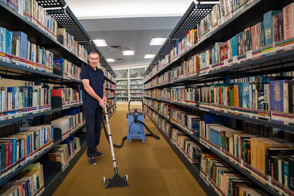 RWS Gebäudeservice Mitarbeiter reinigt mit einem Sprühextraktionsgerät den Textilboden in einer Universitätsbibliothek im Rahmen der Grundreinigung
