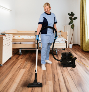 Reinigungskraft saugt den Boden in einem Patientenzimmer