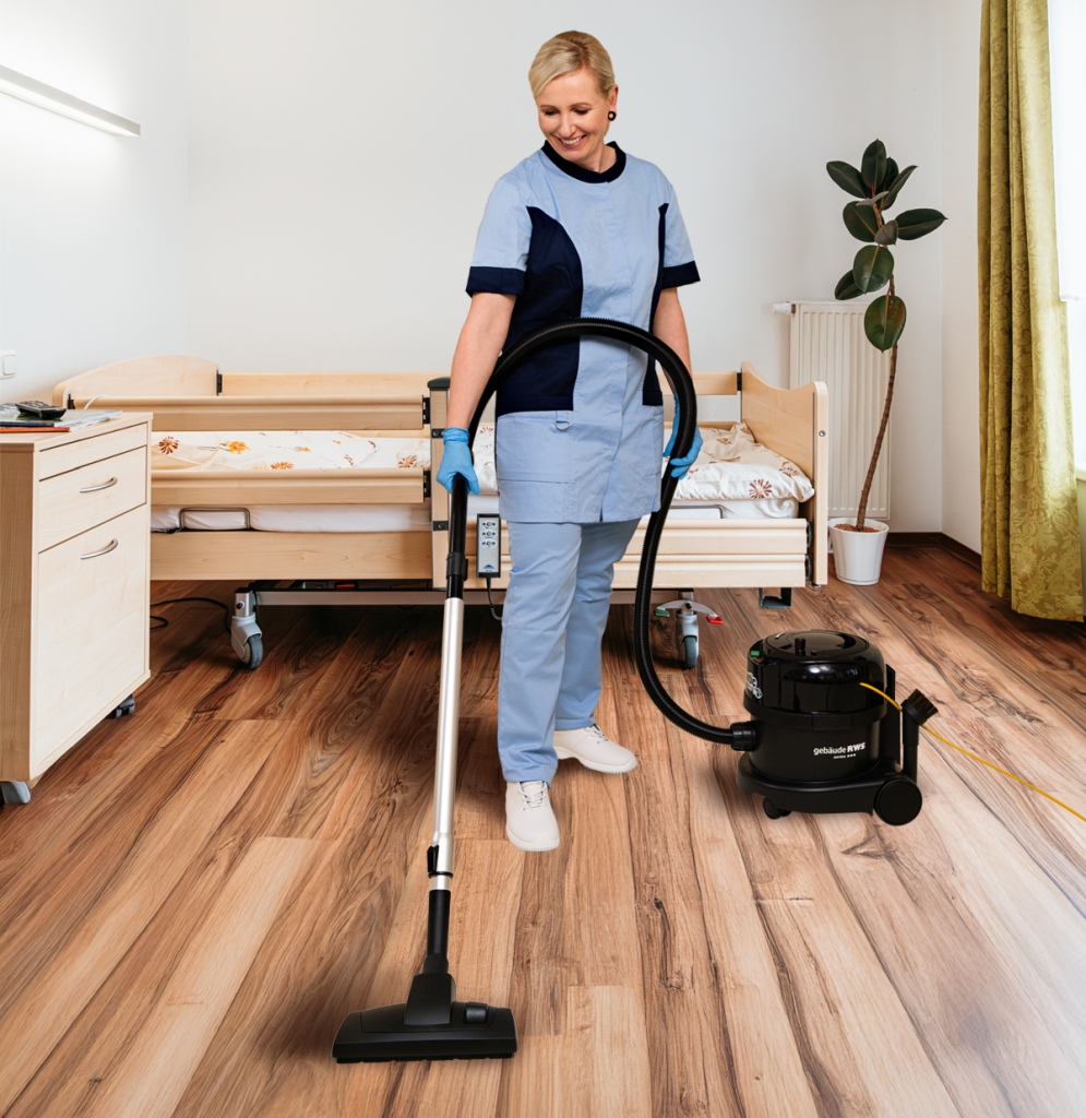 Reinigungskraft saugt den Boden in einem Patientenzimmer