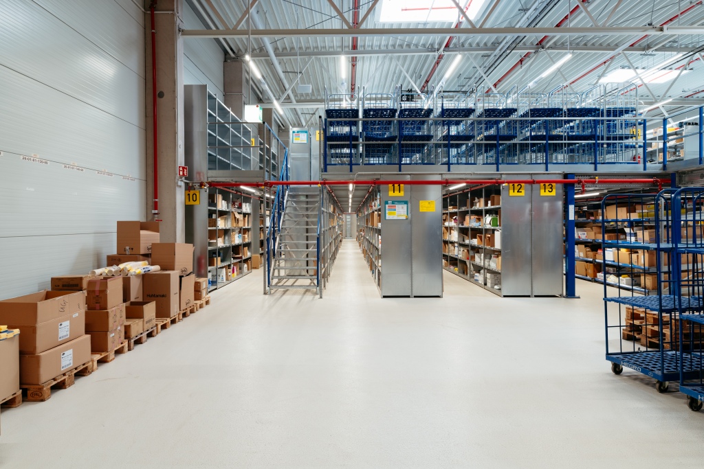Große, aufgeräumte Lagerhalle mit hohen Regalen, Paletten und Rollwagen in einer modernen Logistikumgebung.