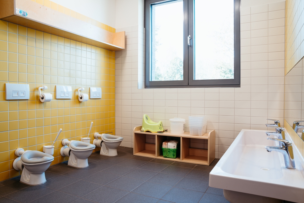 Sanitärbereich einer Kita mit Waschbecken, Spiegel und kindgerechten Toiletten