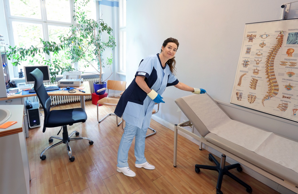 RWS Gebäudeservice Mitarbeiterin reinigt Behandlungsraum einer Arztpraxis für hygienische Sauberkeit.