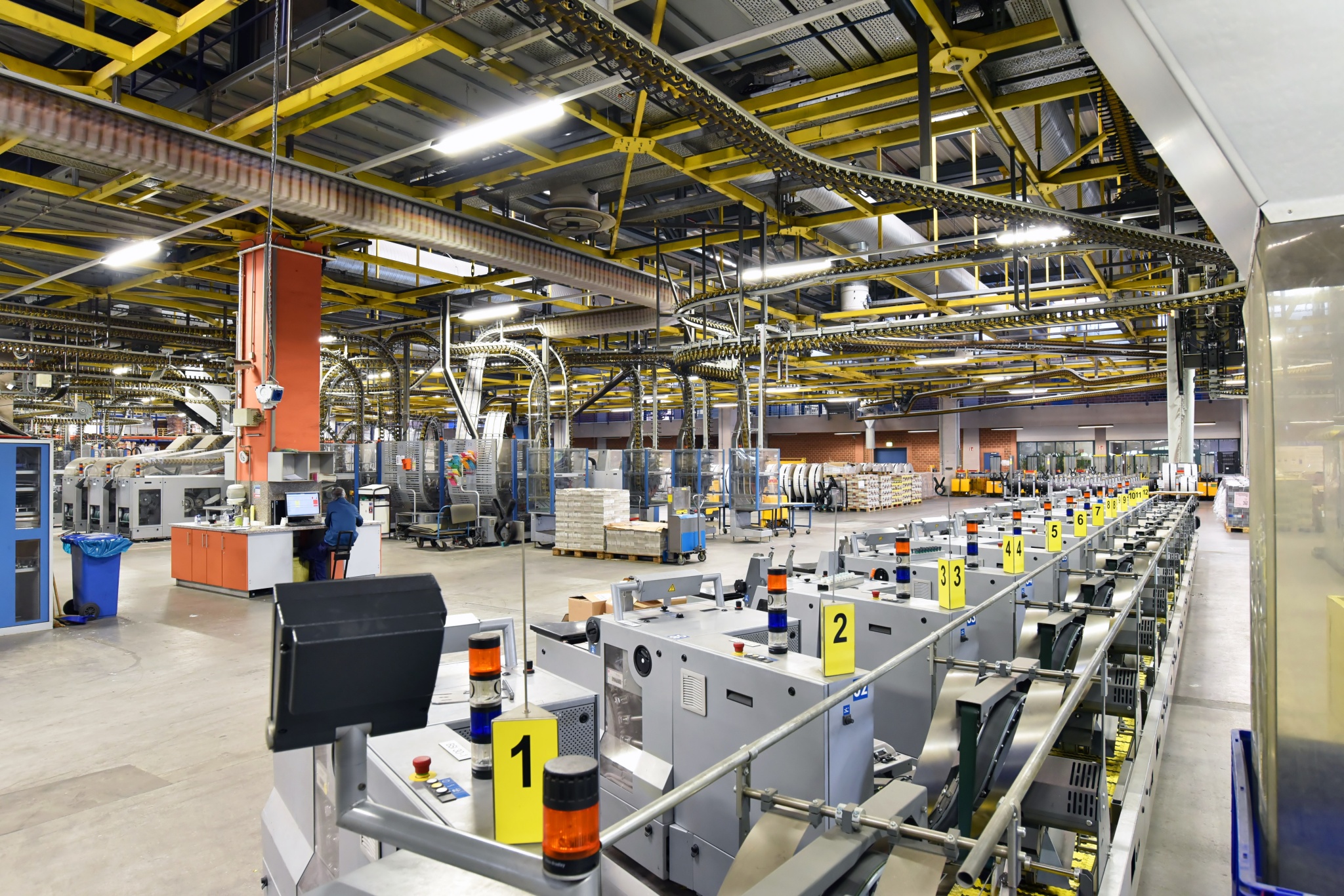 Große Produktionshalle mit Maschinen, Förderanlagen und nummerierten Arbeitsstationen.