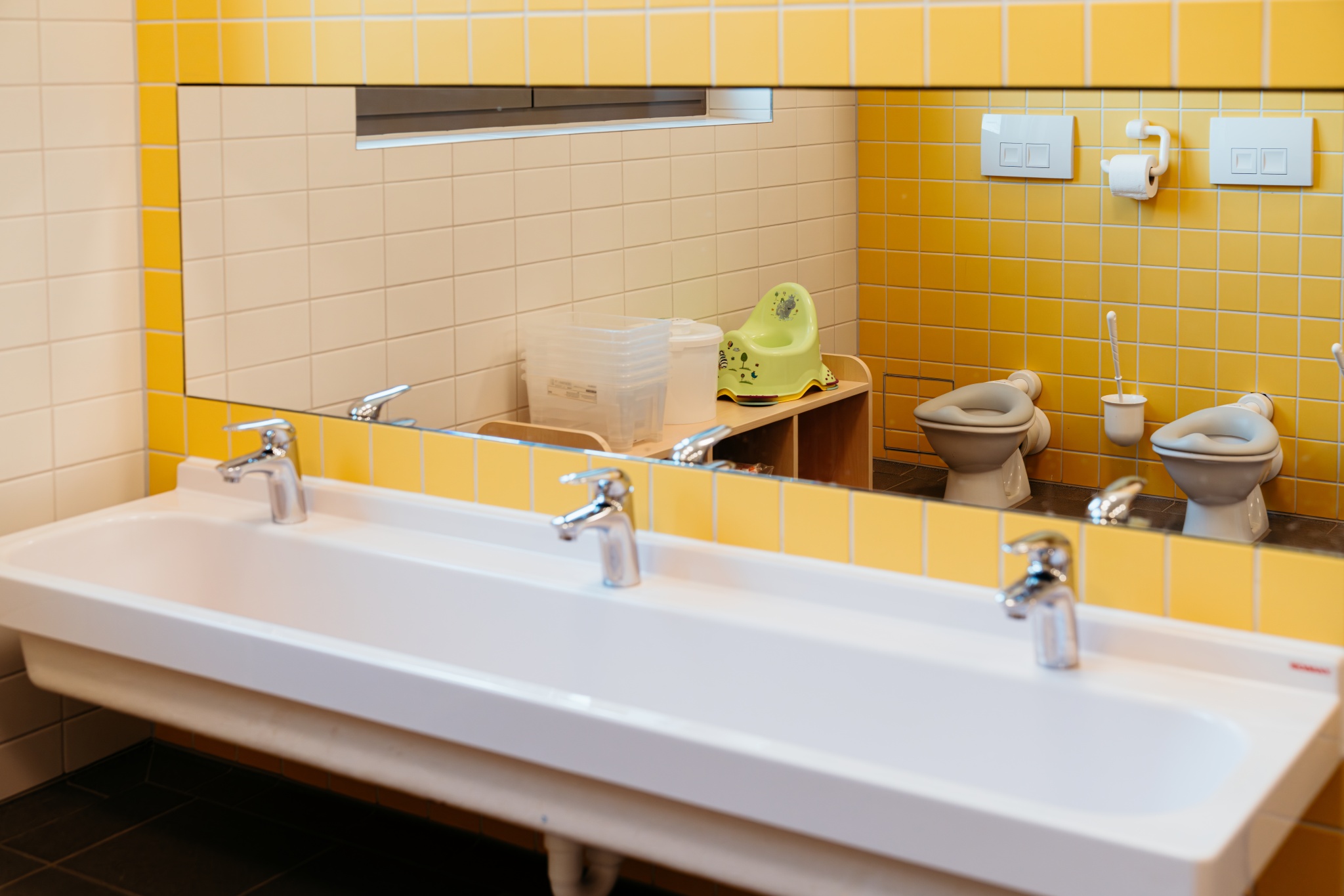 Sanitärbereich einer Kita mit Waschbecken, Spiegel und kindgerechten Toiletten