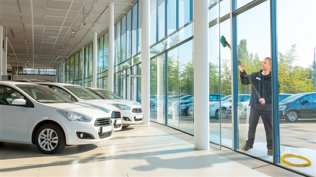 Mitarbeiter von RWS Gebäudeservice reinigt mit professionellem Werkzeug die Fenster eines Autohauses.
