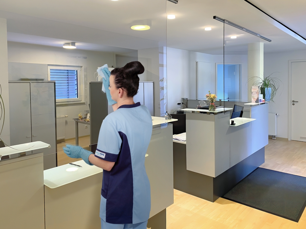 RWS Gebäudeservice Mitarbeiterin reinigt Empfangsbereich einer Arztpraxis für saubere und hygienische Oberflächen.