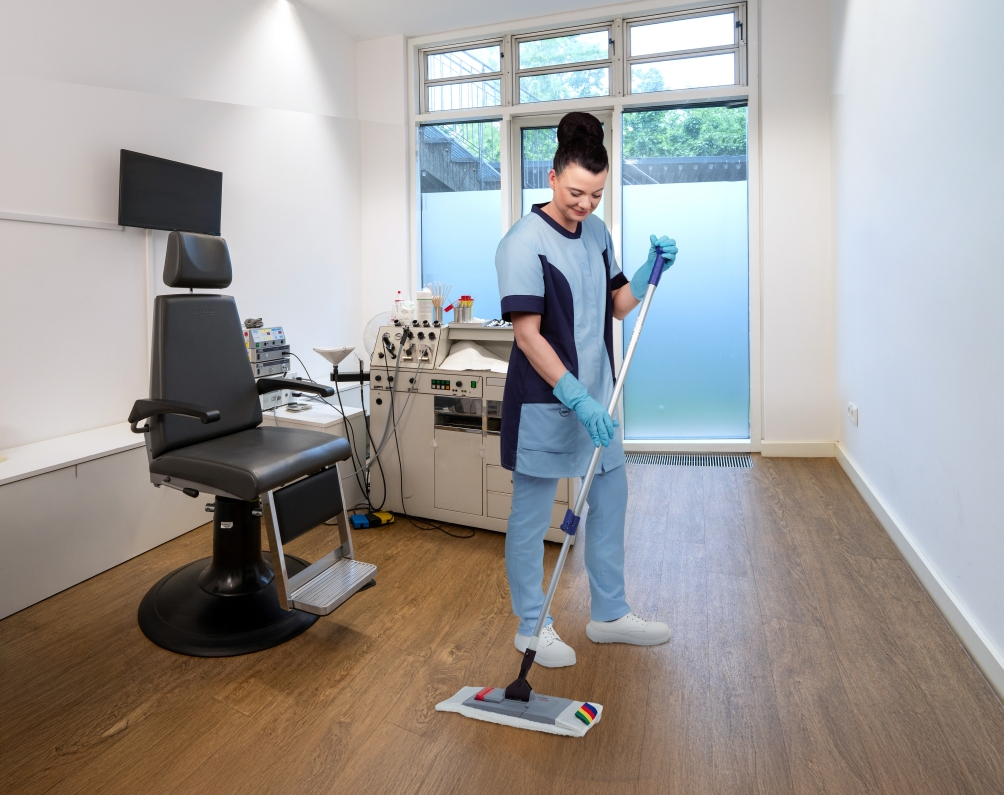 RWS Gebäudeservice Mitarbeiterin reinigt Oberflächen in Behandlungsraum einer Arztpraxis für maximale Hygiene.